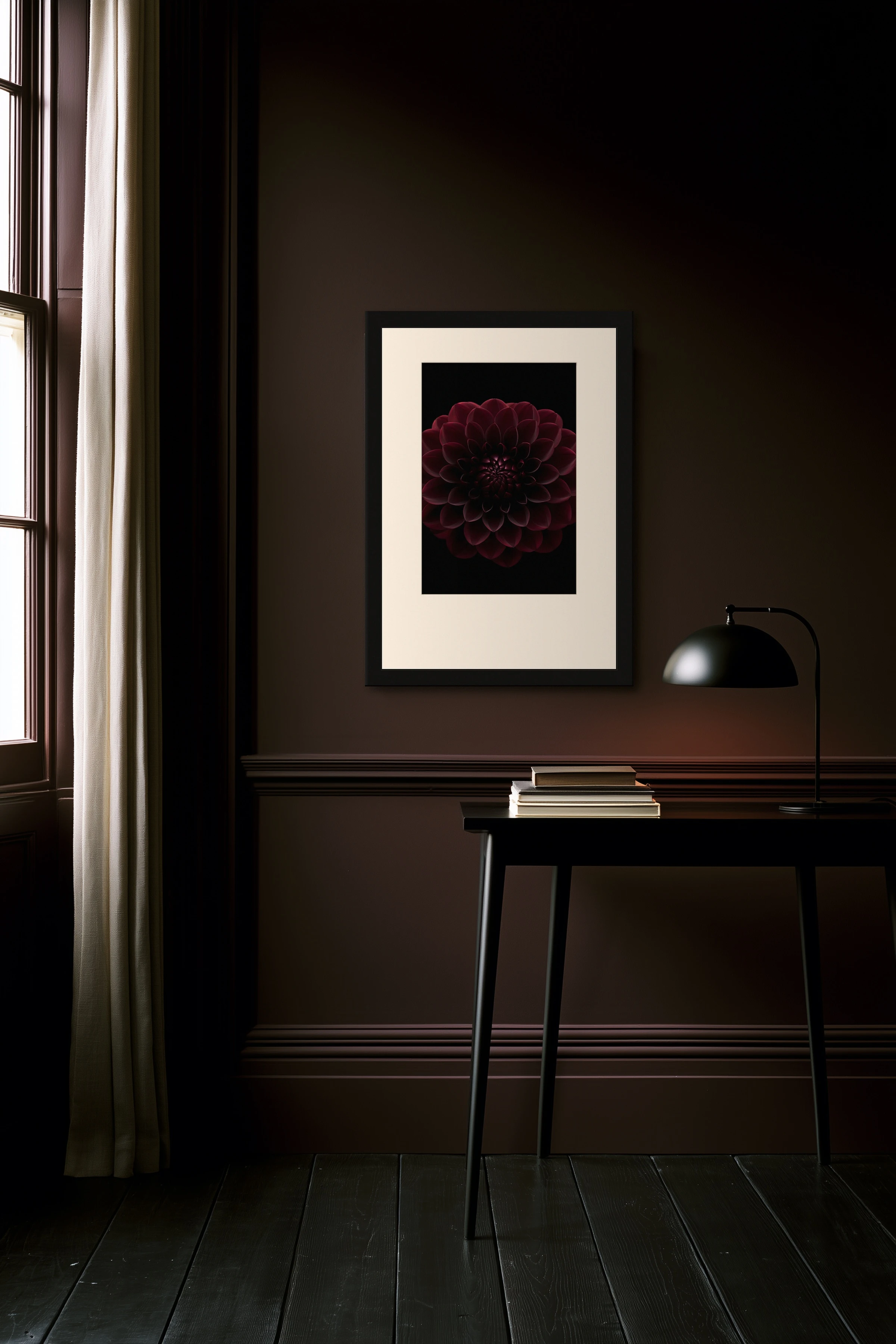 Framed black dahlia print with a wide cream mat and black frame on a deep oxblood wall, black side table with books and an arc lamp below