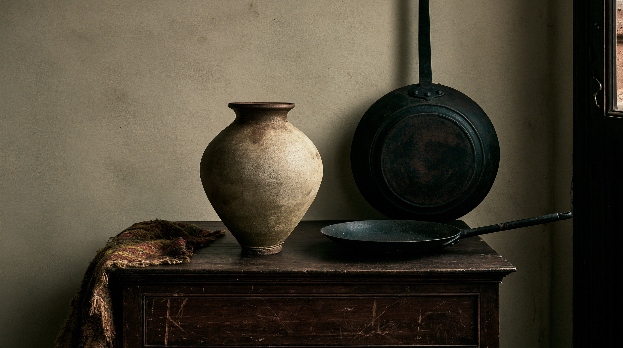 Heritage still life with seasoned cast iron and an unglazed stoneware crock in low window light